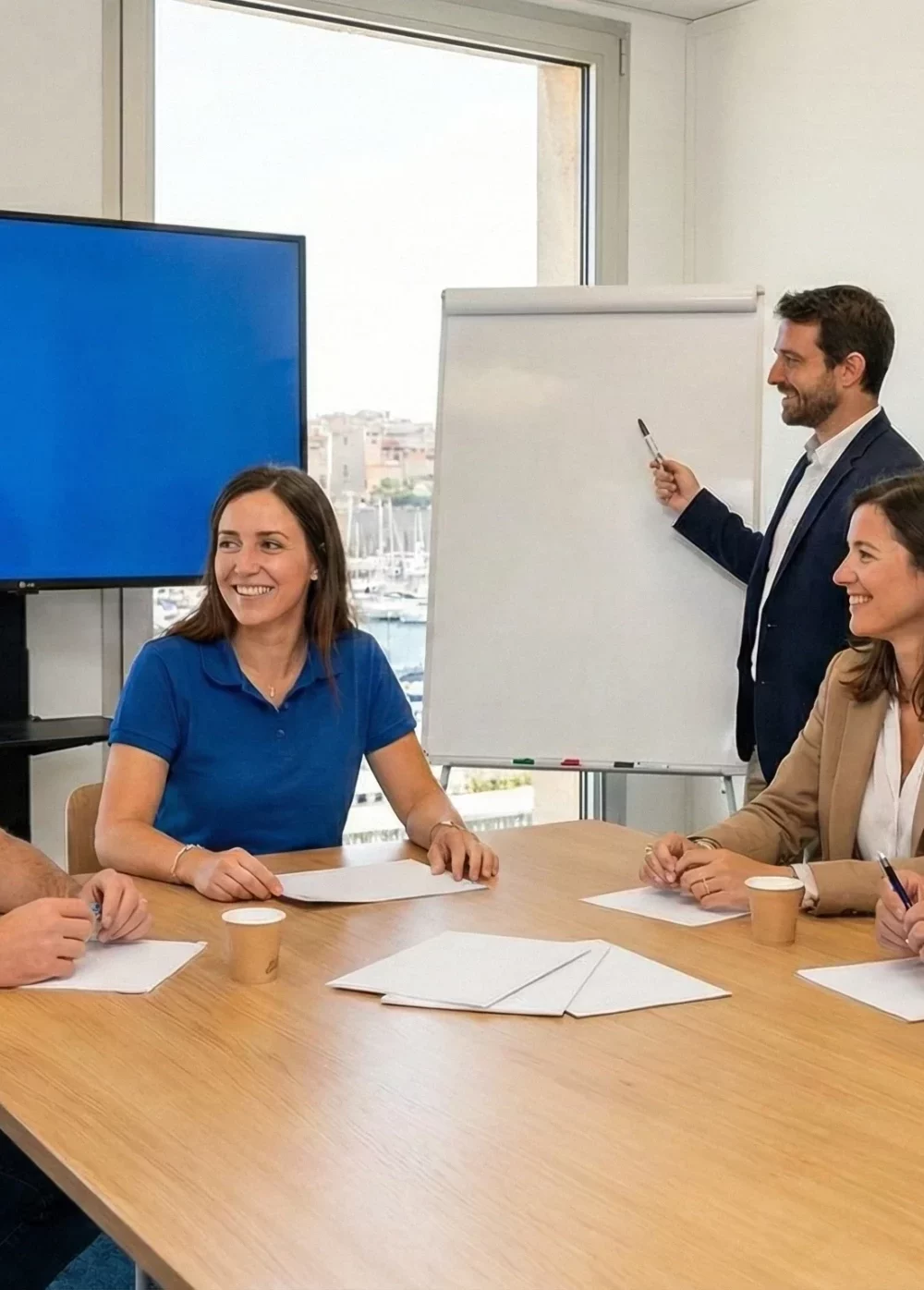 Image d'une réunion avec 5 personnes autour d'une table qui regardent une projection sur un écran